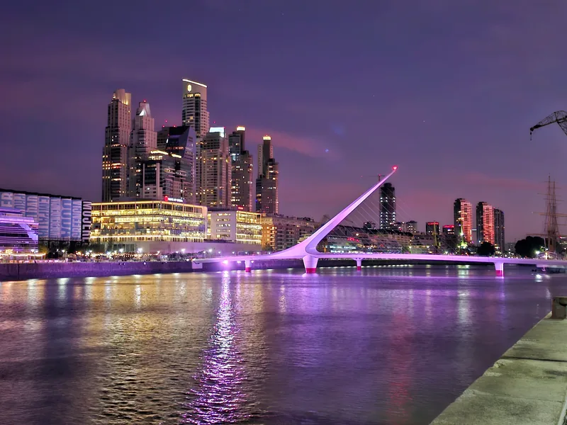 Vista noturna de Puerto Madero, em Buenos Aires, com prédios iluminados e uma ponte sobre a água.