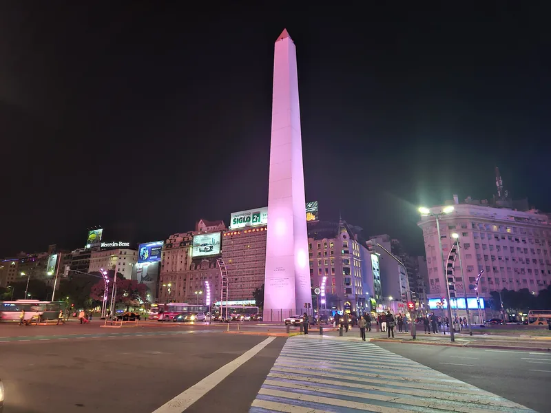 Avenida do centro de Buenos Aires à noite, com um monumento iluminado ao fundo.