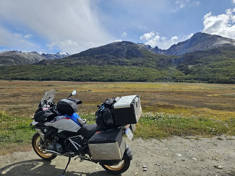 Motocicleta carregada com malas e baú, em uma paisagem de montanhas.