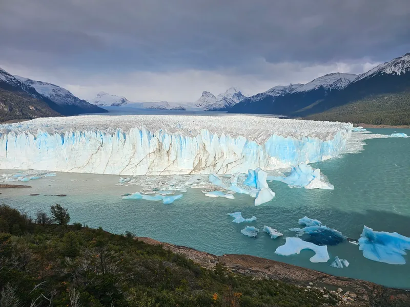 Panorama do Glaciar Perito Moreno, com gelo, lago e vegetação ao redor.