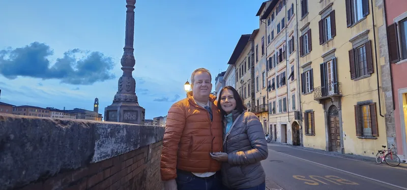 Casal em primeiro plano numa rua de Pisa, ao entardecer.