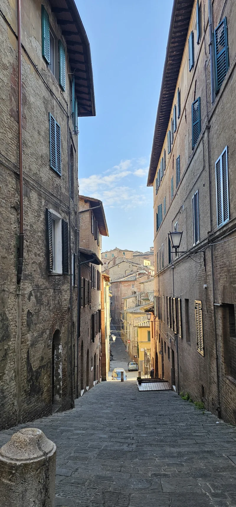 Rua medieval estreita entre fachadas de pedra, em Siena.