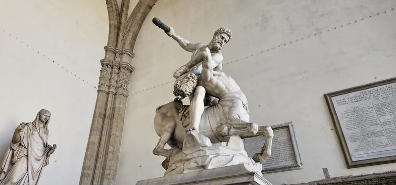 Escultura de mármore branco de um homem lutando com um centauro, sob os arcos de uma loggia, em Florença.