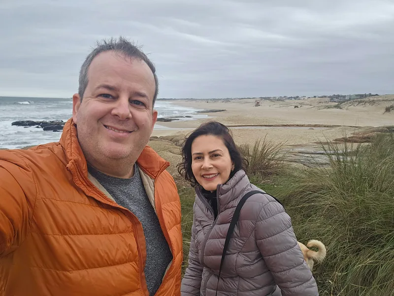 Casal em selfie num mirante de dunas, com praia e mar ao fundo.