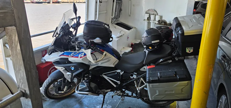 Moto BMW no convés de uma balsa, ao lado de um carro e de um poste amarelo.