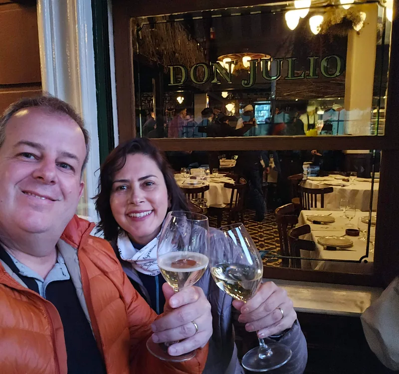 Casal brindando com taças de espumante diante da vitrine do Don Julio.