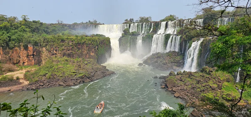 Vista panorâmica das Cataratas do Iguaçu pelo lado argentino, com um barco de turismo no rio.