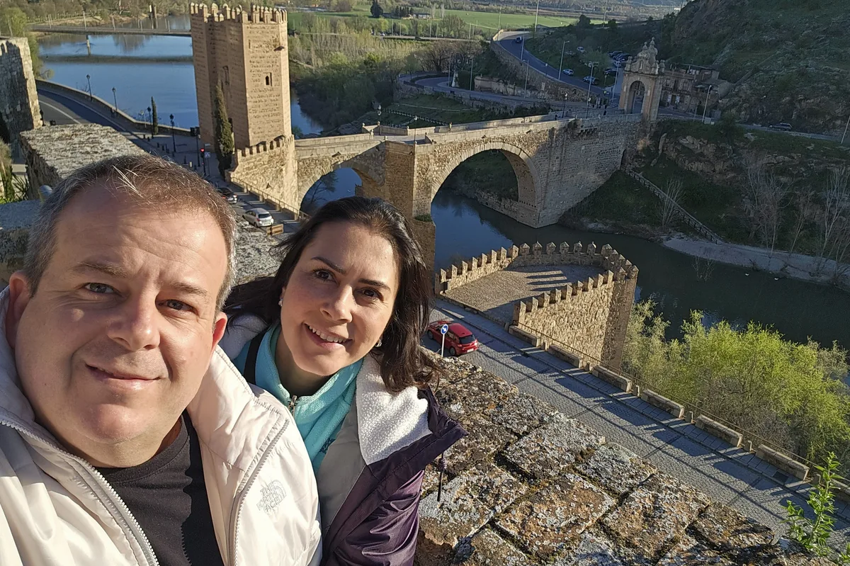 Casal em primeiro plano; contexto urbano ao fundo.